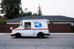 USPS mail truck driving on the road out of frame to the left. The care is moving making it look blurry in the picture.