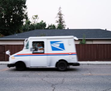 USPS mail truck driving on the road out of frame to the left. The care is moving making it look blurry in the picture.