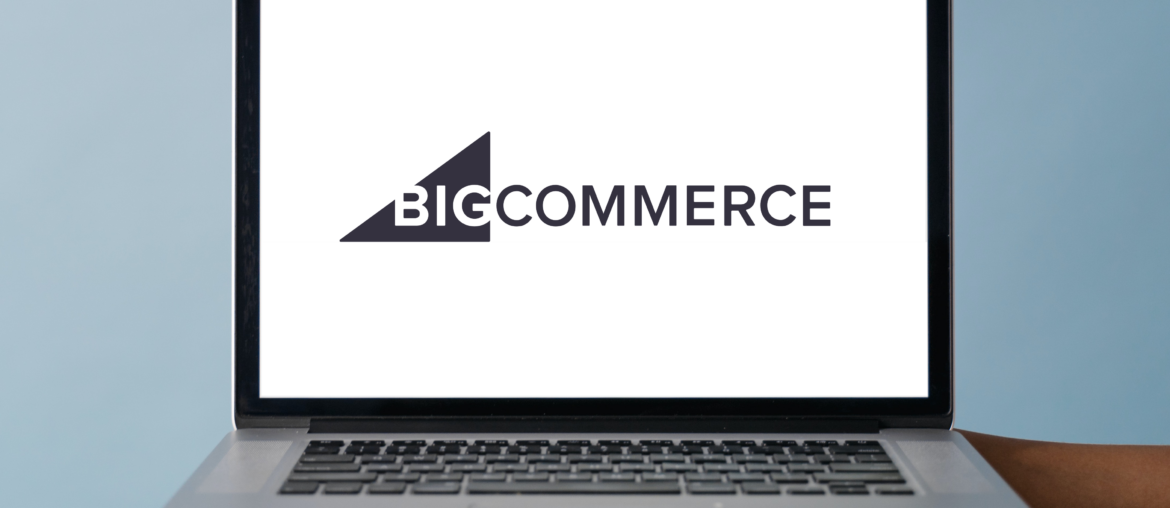 Two hands holding up the base of a mac laptop. On the screen fo the laptop is the logo for BigCommerce.